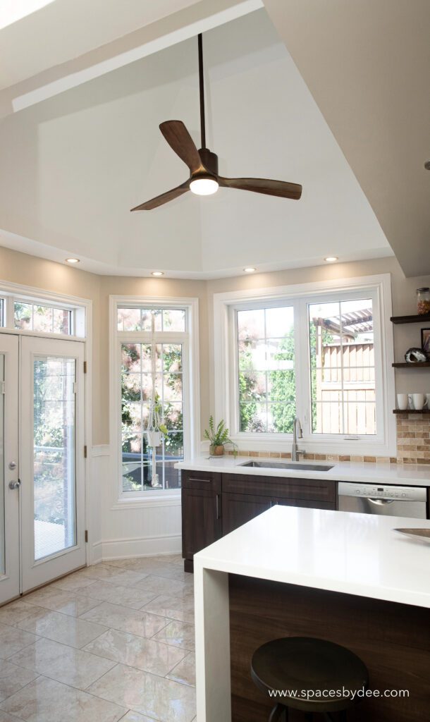 Large family-style kitchen with waterfall island, vaulted ceiling with fan, color scheme is white, brown and beige.