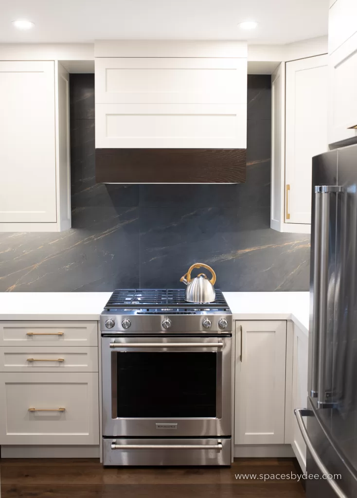 beautiful moody and bold kitchen with black, white, cream and gold accents with a bold backsplash and brown wood flooring.