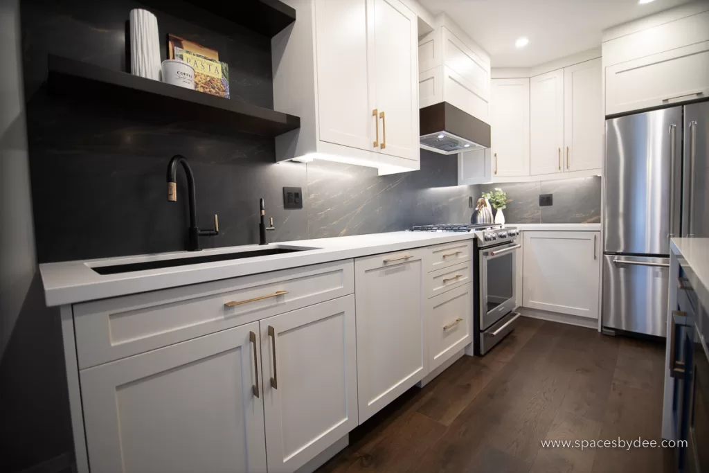 beautiful moody and bold kitchen with black, white, cream and gold accents with a bold backsplash and brown wood flooring.