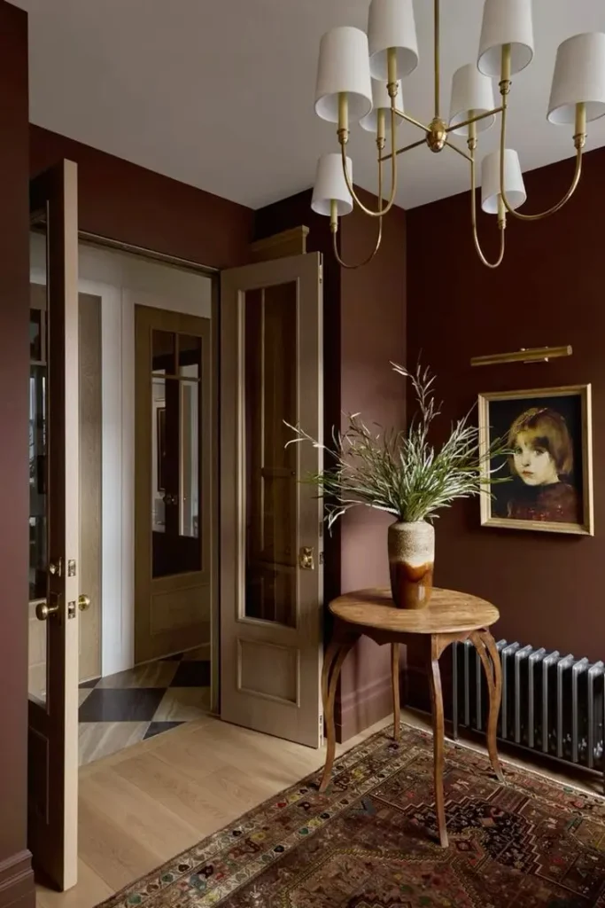 Small entry painted a rich burgundy brown with a brass chandelier, round wood side table and vintage rug