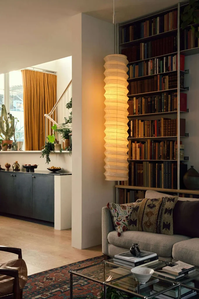 Small living room with floor-to-ceiling bookshelves and a tall paper floor lamp drawing the eye upward